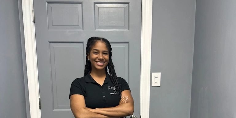 Smiling woman with braided hair stands confidently in front of a gray door.