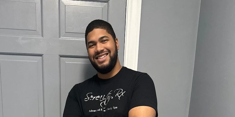 Smiling man stands confidently with arms crossed in front of a gray door.